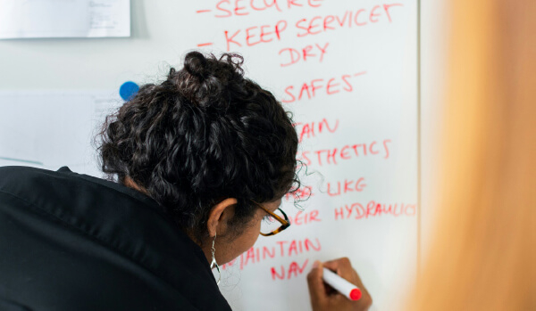 A person writing on a whiteboard with a red marker, listing tasks and instructions.