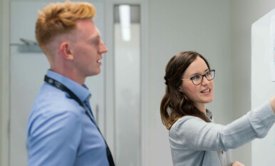 Two people dressed in smart office wear are writing on a white board.