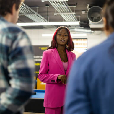 A woman in a pink suit stands and talks to two people in a casual setting.