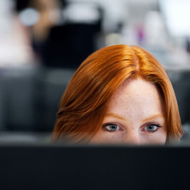 A close-up of a person with red hair looking intently at a computer screen.