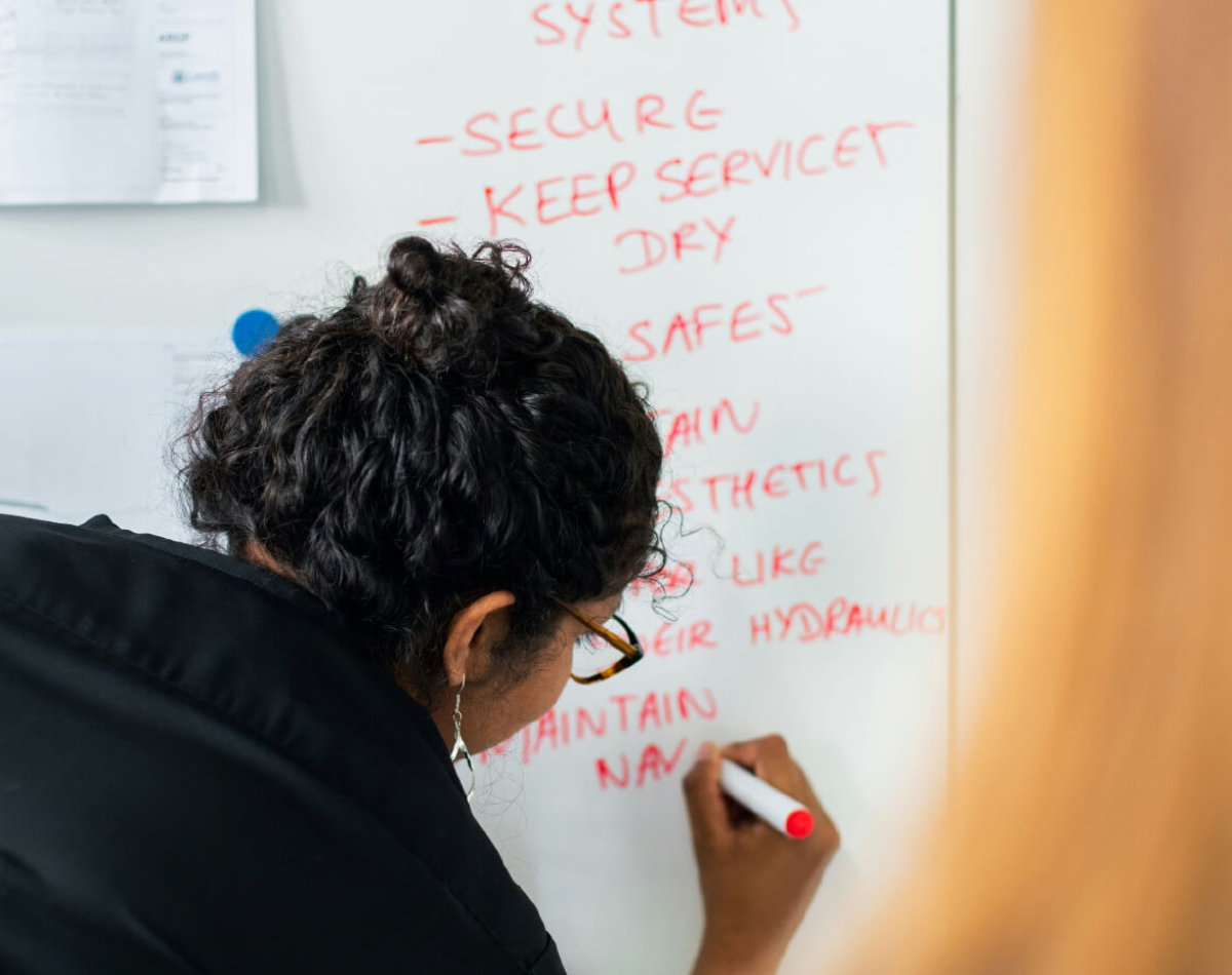 A person writing on a whiteboard with a red marker, listing tasks and instructions.