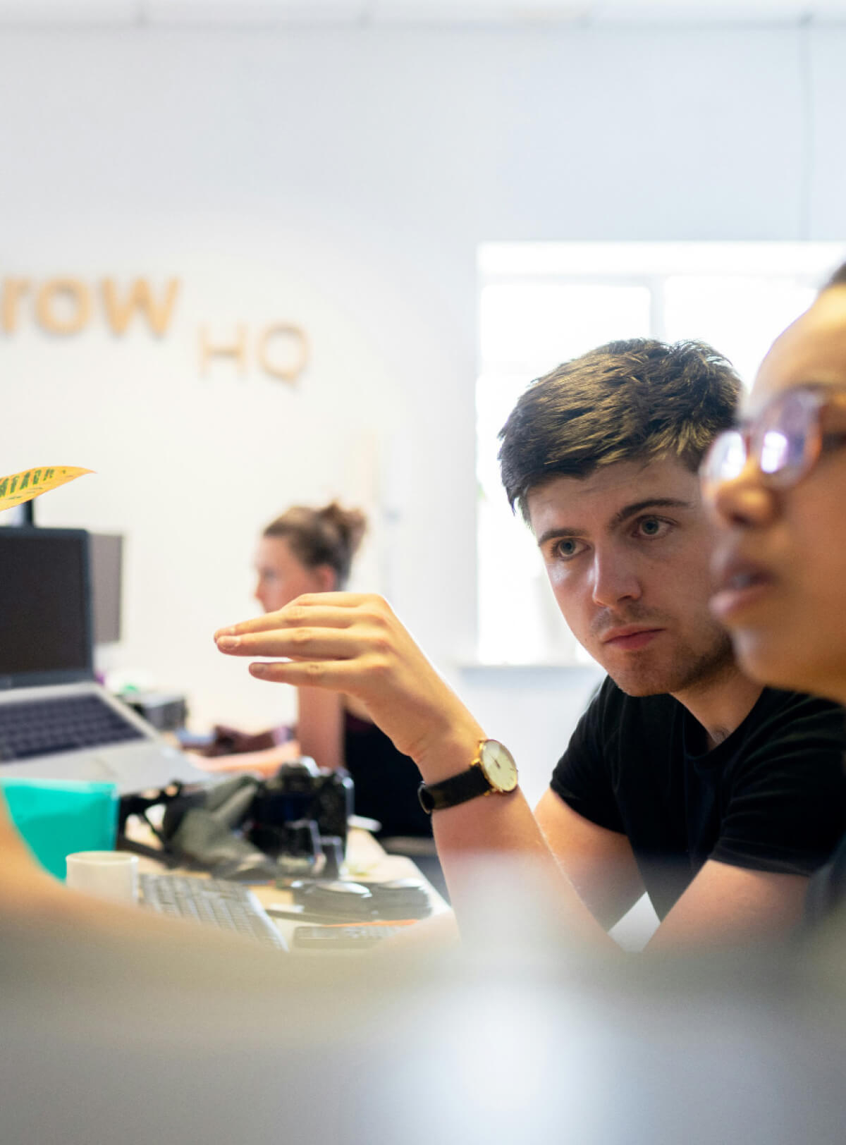 Two people engaged in conversation whilst working at a computer in an office setting.