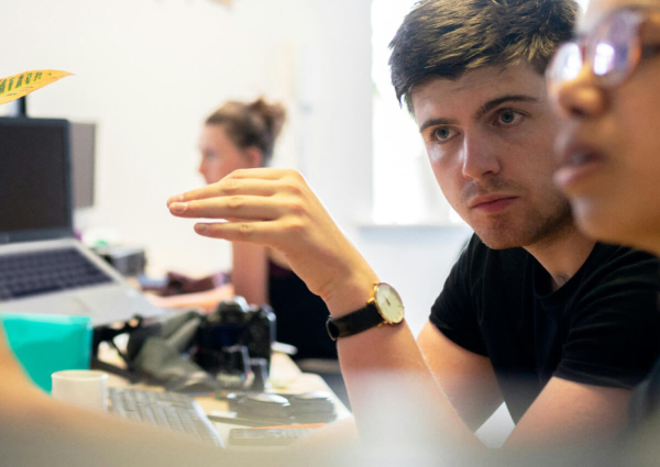 Two individuals engaged in a discussion at a workspace, with one person gesturing while the other listens.