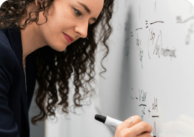 A woman writes mathematical equations on a whiteboard.