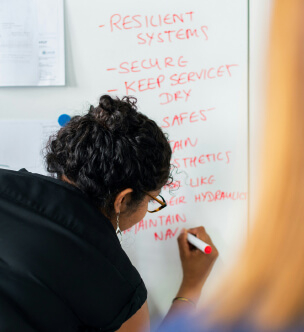 A person writing on a whiteboard with a red marker, listing tasks and instructions.