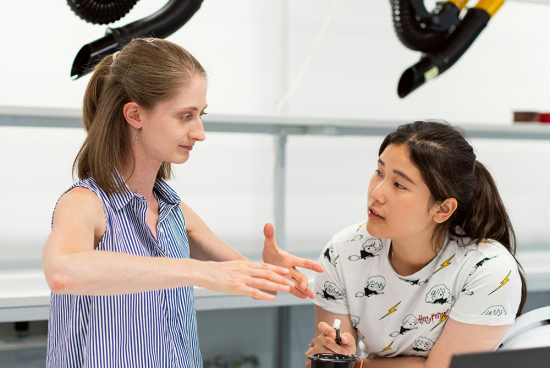 A teacher explains a concept to a student in a robotics workshop.