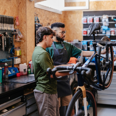 Two people are stood in a workshop repairing a bicycle.