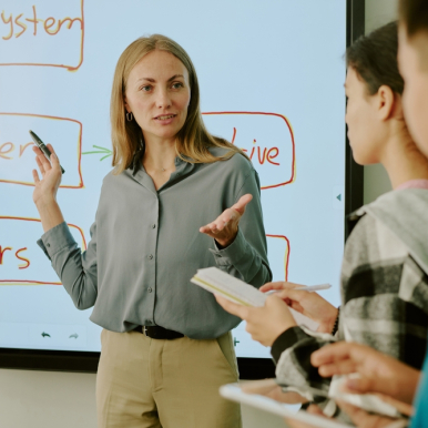 A female instructor is stood in front of several students explaining a concept.
